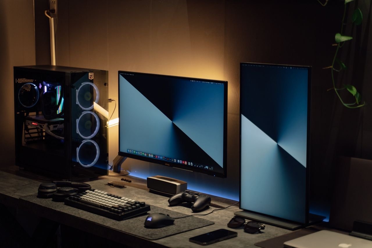 Services Modern dual monitor PC setup with tech gadgets on a sleek desk in a dimly lit room.